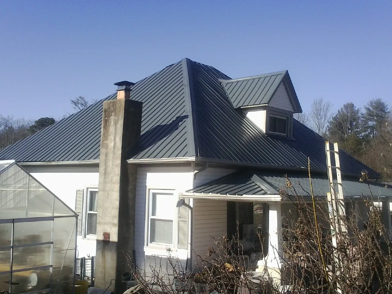 Dark blue standing seam metal roof on a white farmhouse with dormer — Slate & Tile Roof Repair by Roofing Brothers in Villanova