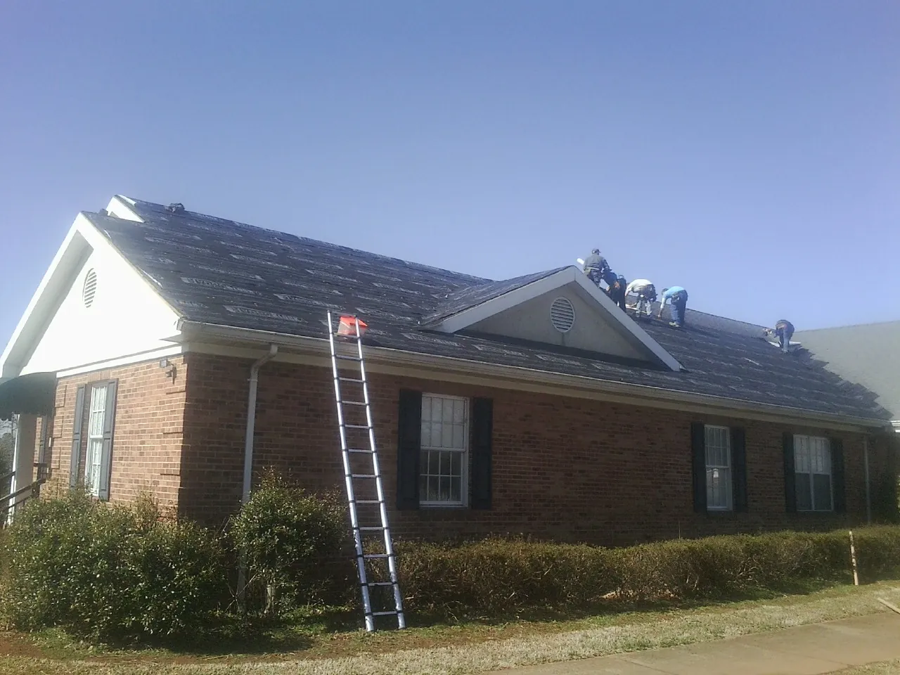 Crew tearing shingles off a brick ranch roof with a ladder set — Metal Roof Repair work by our crew in Villanova