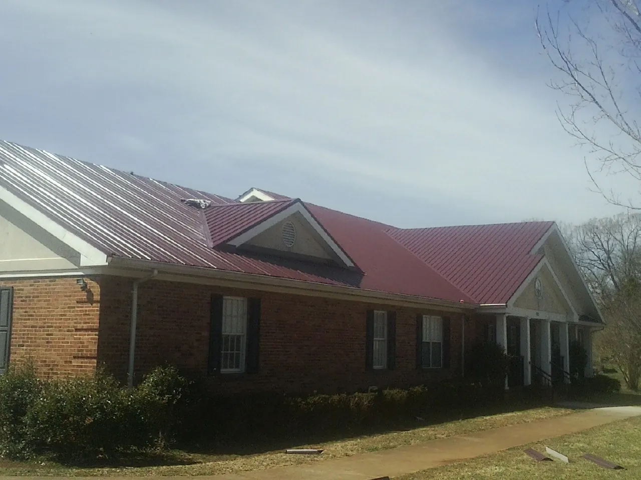 Red metal roof with gabled entries on a long brick building, from a Hail Damage Roof Repair job in Villanova