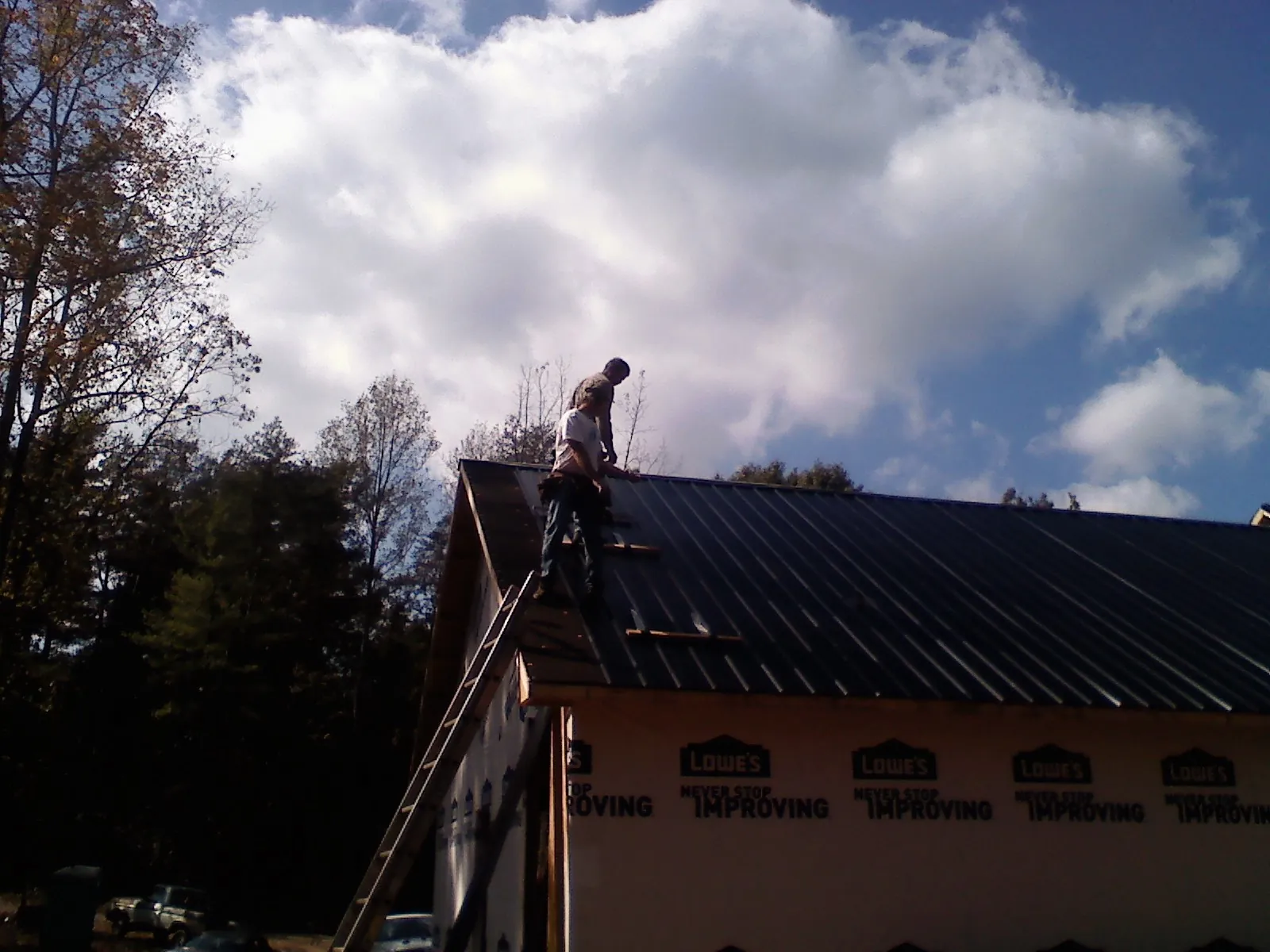 Roofer fastening dark metal panels high against a cloudy sky, from a Roof Inspection job in Villanova