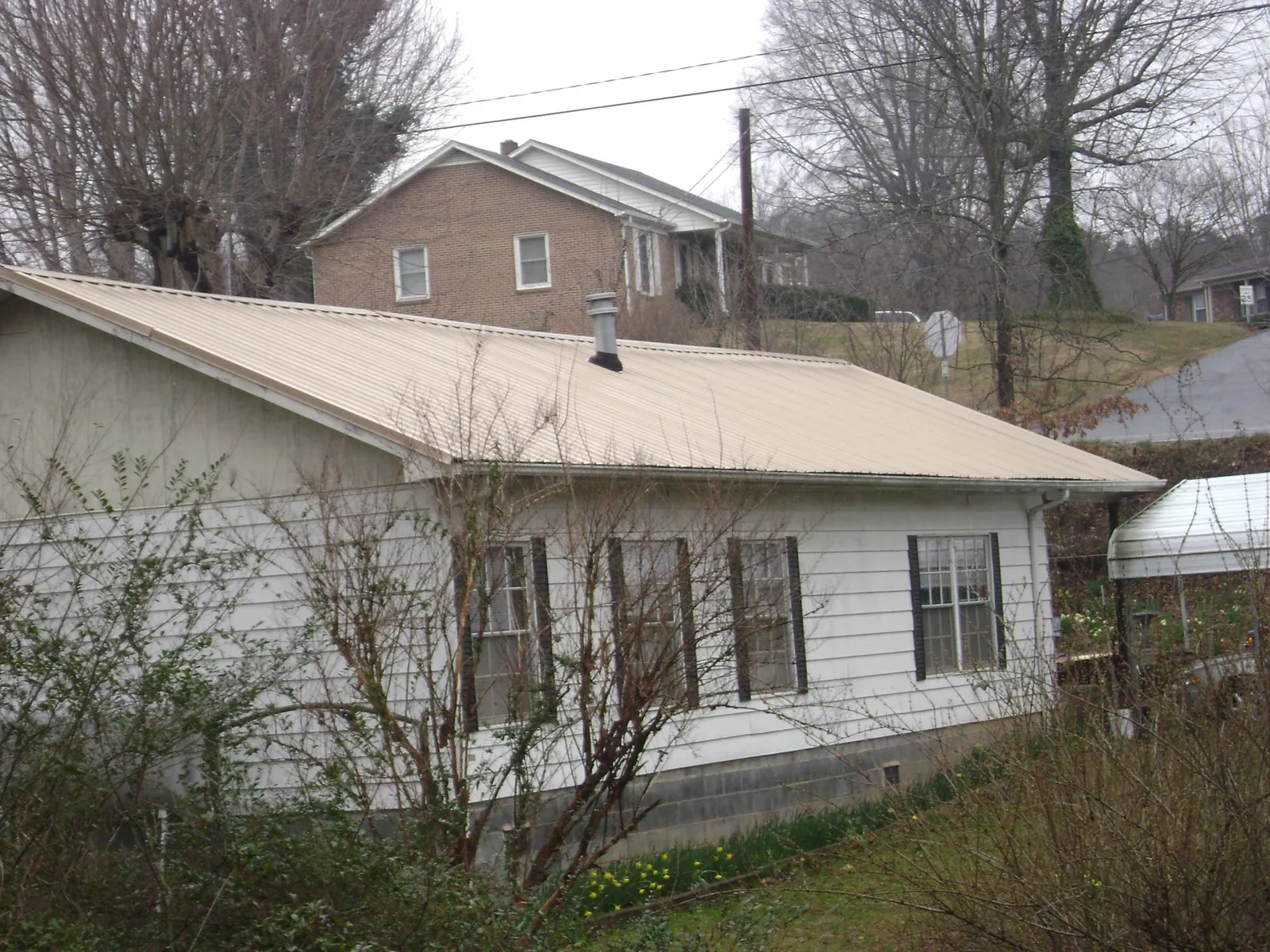 Tan metal roof on a white sided house set into a hillside — Commercial Roofing by Roofing Brothers in Villanova